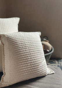 Two cream colored textured pillows on a couch. 