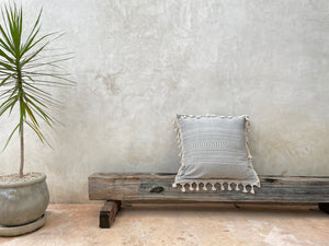 Large artisan floor pillow with tassle fringe. Gray and natural white pillow. Displayed at architectural boutique hotel.