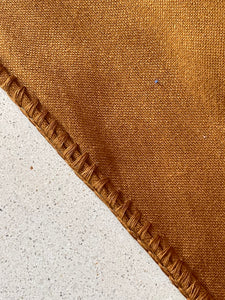 Embroidered stitch detail on golden terracotta blanket.