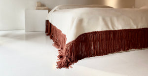 Cotton blanket with handmade rust fringe in architectural space.