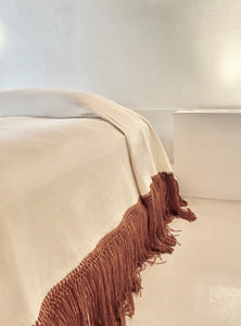 Cotton blanket with rust  terracotta colored fringe in architectural space in Mexico.