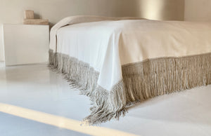 Handwoven cotton blanket with gray putty draping fringe in architectural space.