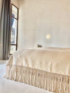 Textured white blanket in architectual space. Bedcover has fringe. Made in Oaxaca Mexico