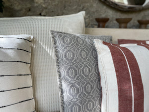 Collection of handmade pillows from Oaxaca arranged on a couch. Throw pillows have black and terracotta stripes next to a natural woven large pillow.