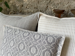 Collection of white and gray pillows against a concrete wall with pottery details.