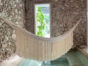 White natural Tulum-style hammock hanging over a pool.