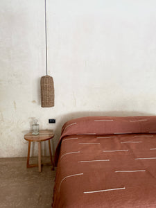 Handwoven blanket made in 100% cotton displayed in an architectural space. Terracotta blanket with white detail.