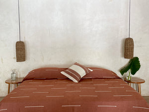 Handwoven blanket made in 100% cotton displayed in an architectural space. Terracotta blanket with white detail.