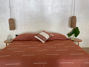 Striped pillow on coordinated handmade luxury bedcover in terracotta rust color.