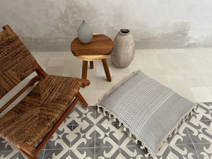 Artisan made large floor pillow in gray and white with textured pattern and fringe tassels displayed on tile floor in villa.