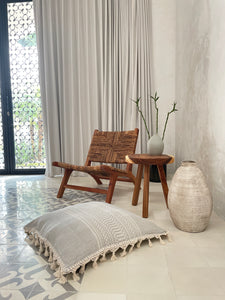 Artisan made large floor pillow in gray and white with textured pattern and fringe tassels displayed on tile floor in villa