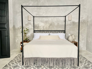 Modern bedroom with handwoven pillow and fringe gra and white blanket. Tiled villa floor.