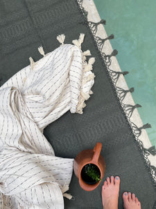 woven green fringe blanket by pool. Displayed with black and white fringe blanket tossed by pool.