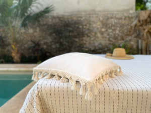 Handwoven floor pillow with fringe tassel poolside in natural white. 